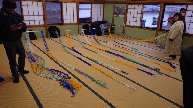 畳の部屋でカラフルな網が長く並べられ、参加者が端を持って準備している写真