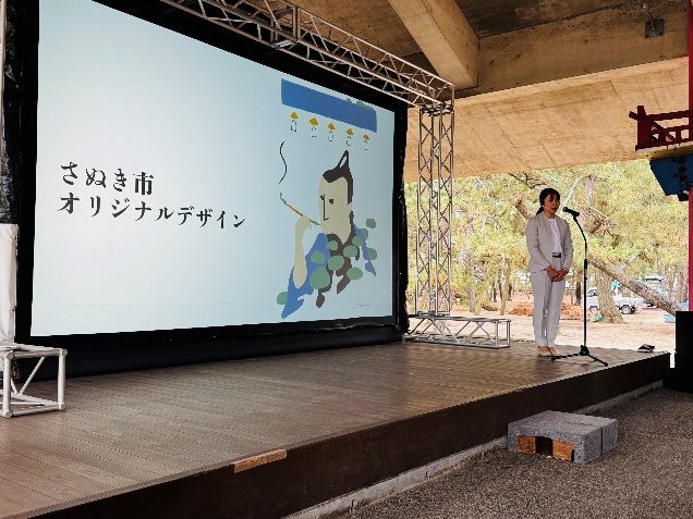 「さぬき市オリジナルデザイン」のスライドを背に女性がマイクで説明している写真
