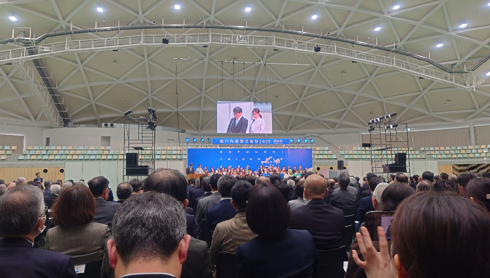 屋内アリーナで大勢の来場者が瀬戸内国際芸術祭2025開会式のステージを見ている写真