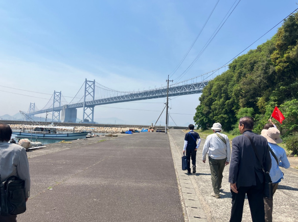 海沿いの道を大きな橋を背景に参加者が旗を持って歩いている写真