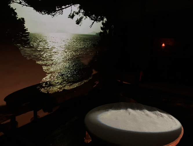 海の映像が投影された暗い部屋に白い円形のオブジェが置かれている写真