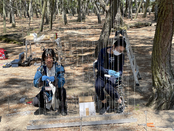 屋外でアート作品のフレームにレンズを取り付けている二人の写真