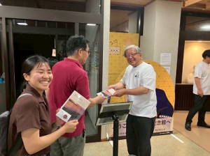 館内入口で白いシャツを着た市長が来館者にパンフレットを手渡している写真