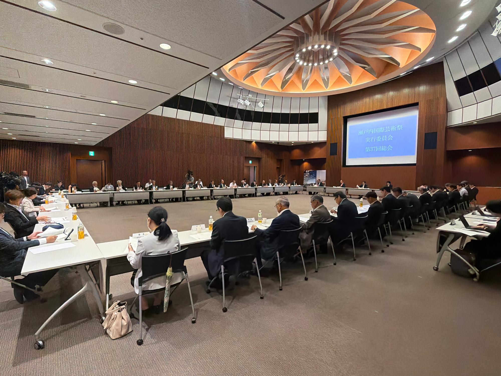 瀬戸内国際芸術祭実行委員会第37回総会の会場にて出席者がロの字に座り話を聞いている写真