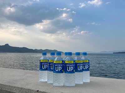 海辺の堤防の上にスポーツドリンクのペットボトルが並び背景に海と雲のかかった空が広がっている写真