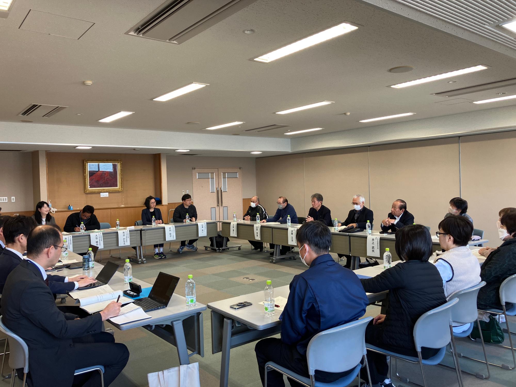 会議室にて意見を発表する女性とその話を聞いている参加者たちの写真