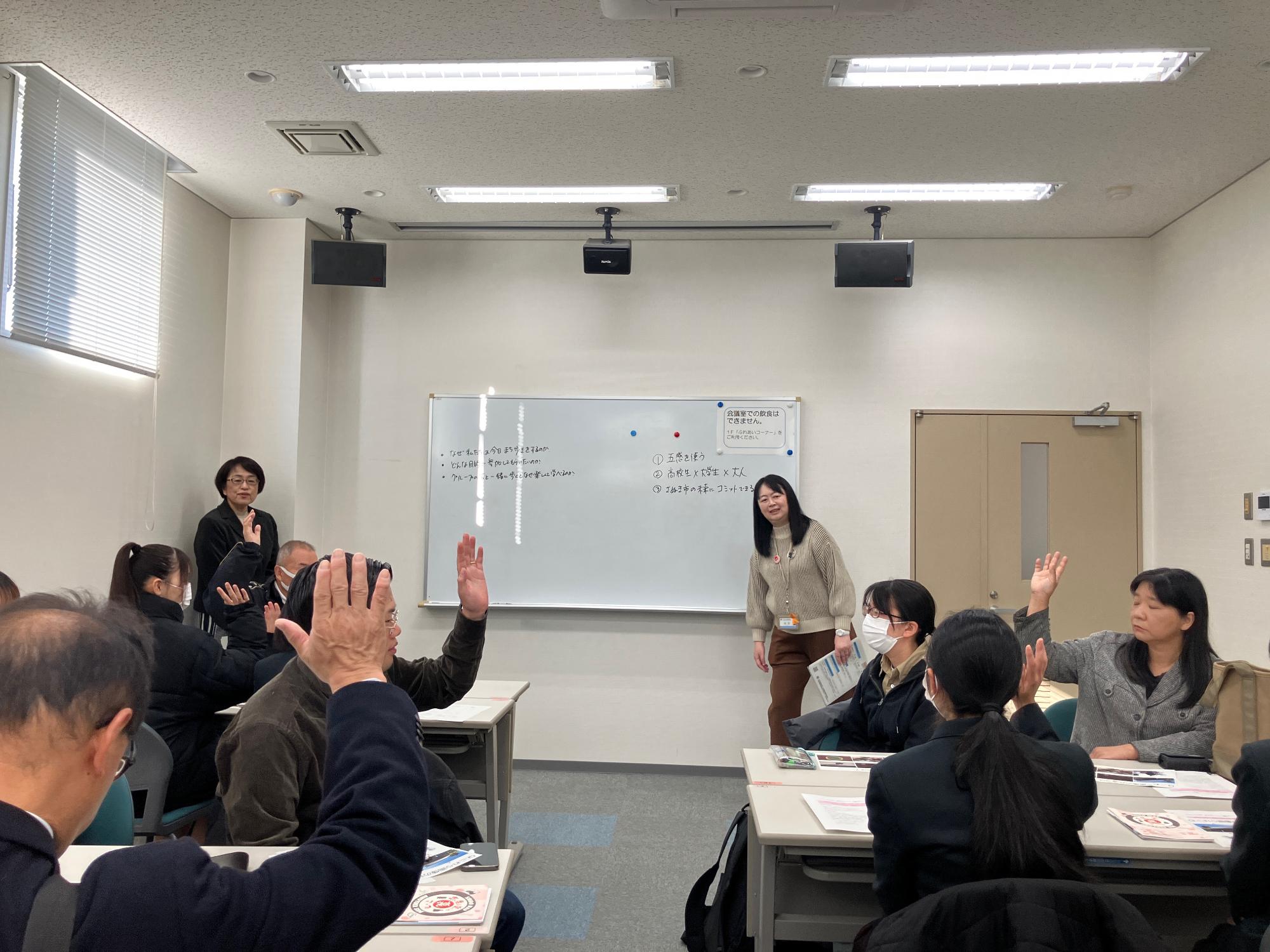 会議室にて呼びかけに応じて挙手を行う参加者の写真