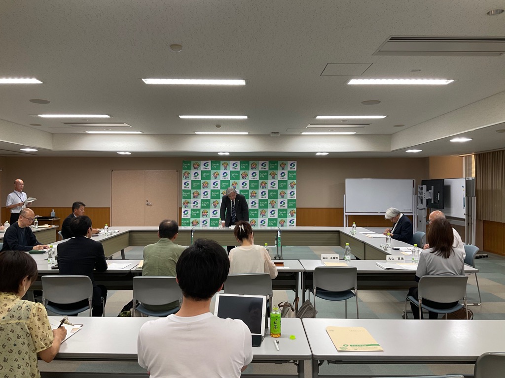 会議室にて挨拶を行っている男性と挨拶を聞く参加者の写真