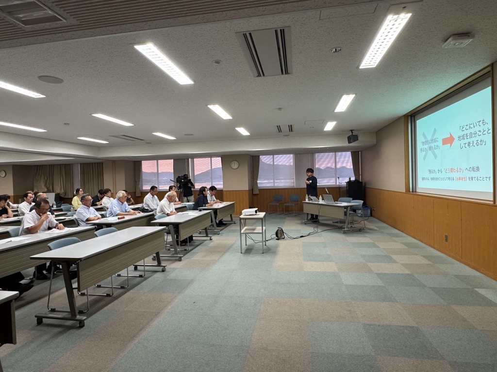 会議室にて講演を行っている男性と講演を聞く参加者の写真