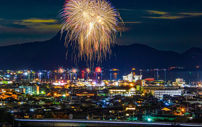 海辺の街の夜景の上空に大輪の花火が打ち上がっている写真