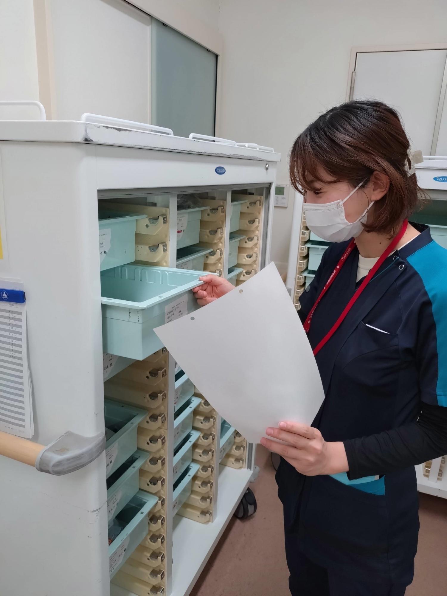 紙を片手に棚のトレーを引き出す女性の写真