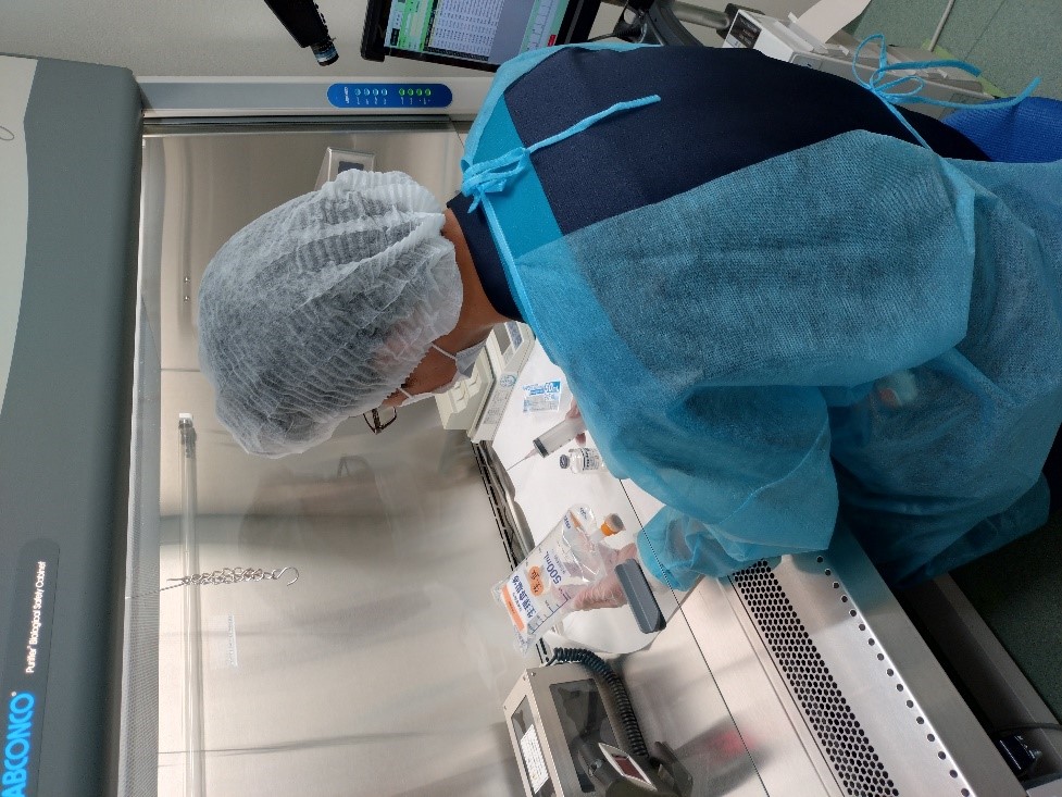 注射器と点滴を持った検査着姿の人の後ろ姿の横向きの写真