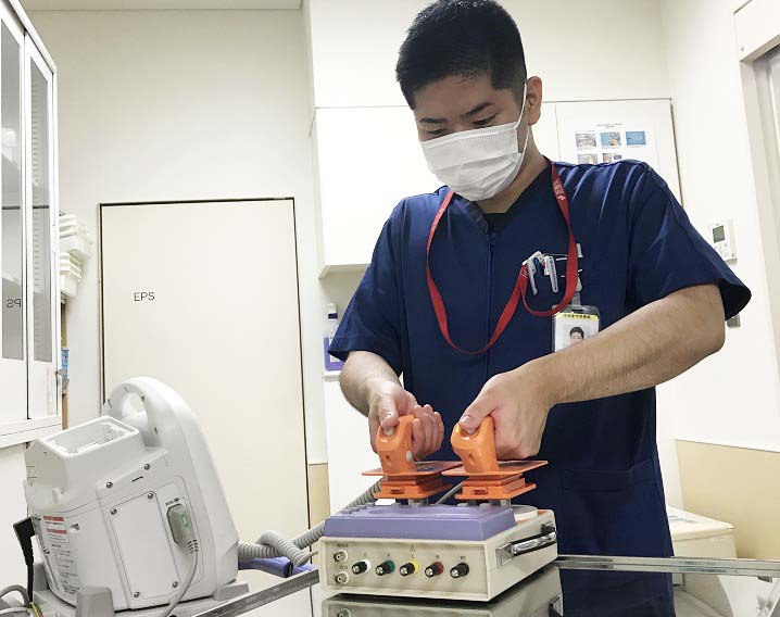 青のスクラブを着た男性が両手でオレンジの機材を操作している写真