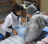 ベッドの縁に座る高齢男性の足を揃えて手を添える女性の写真