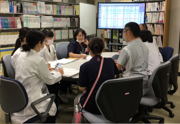 本棚に囲まれた机で会議をしている人たちの写真