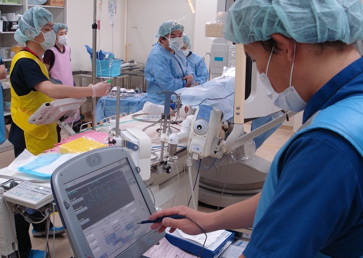 メディカルキャップを付けた人がタッチペンでモニターを操作している写真