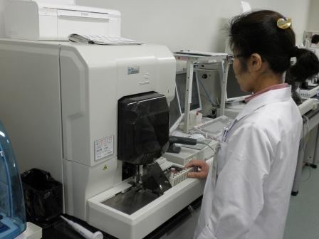 検査機器の前に立つ白衣姿の女性の写真