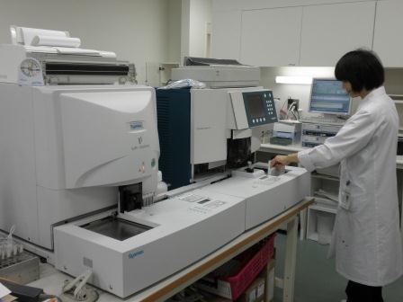 機械の前に立ち、操作する白衣姿の女性の写真