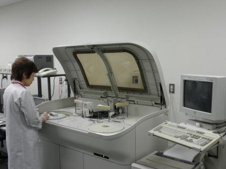 ふたの付いた大きな機械の前に立つ白衣姿の女性の写真