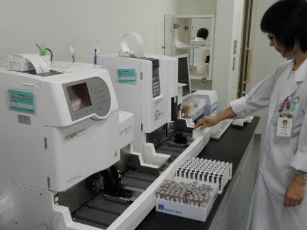 台の上に乗った機械に触れている白衣姿の女性の写真