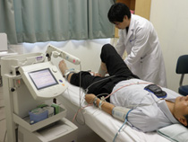 胸に機械をつけ、横になった男性の足を触る白衣姿の男性の写真