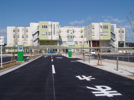 手前に駐車場、奥に白と薄緑に塗られた4階建ての建物がある写真