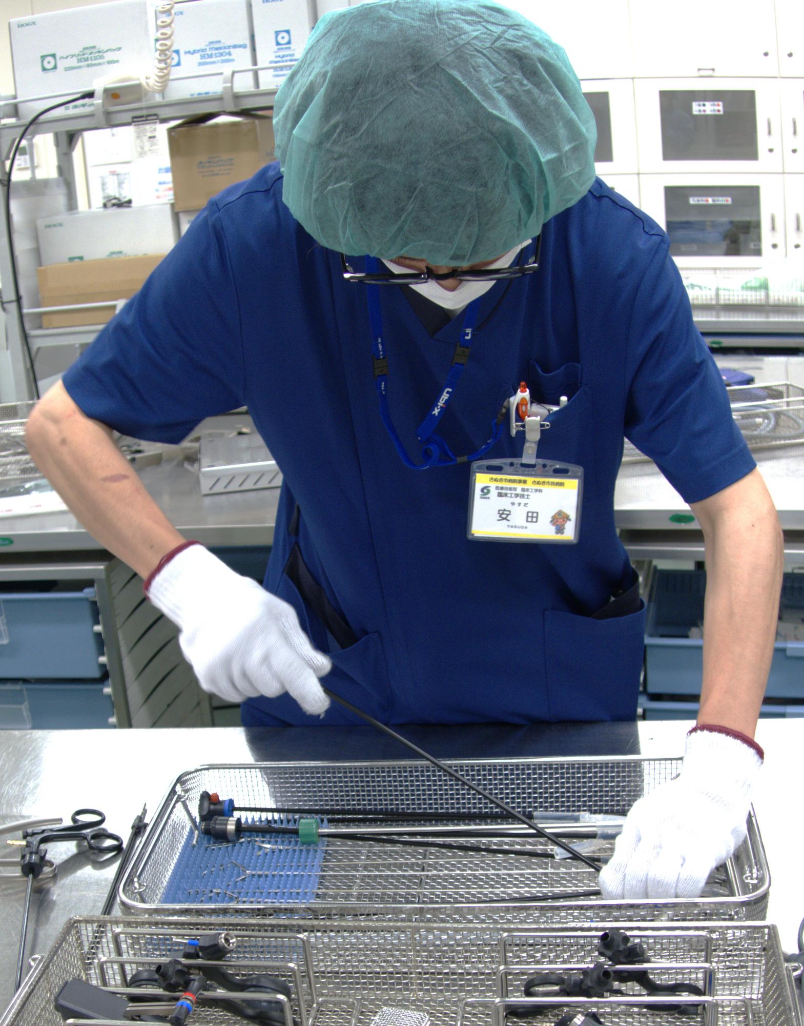 メディカルキャップを付けた人が軍手で細長い棒を扱っている写真