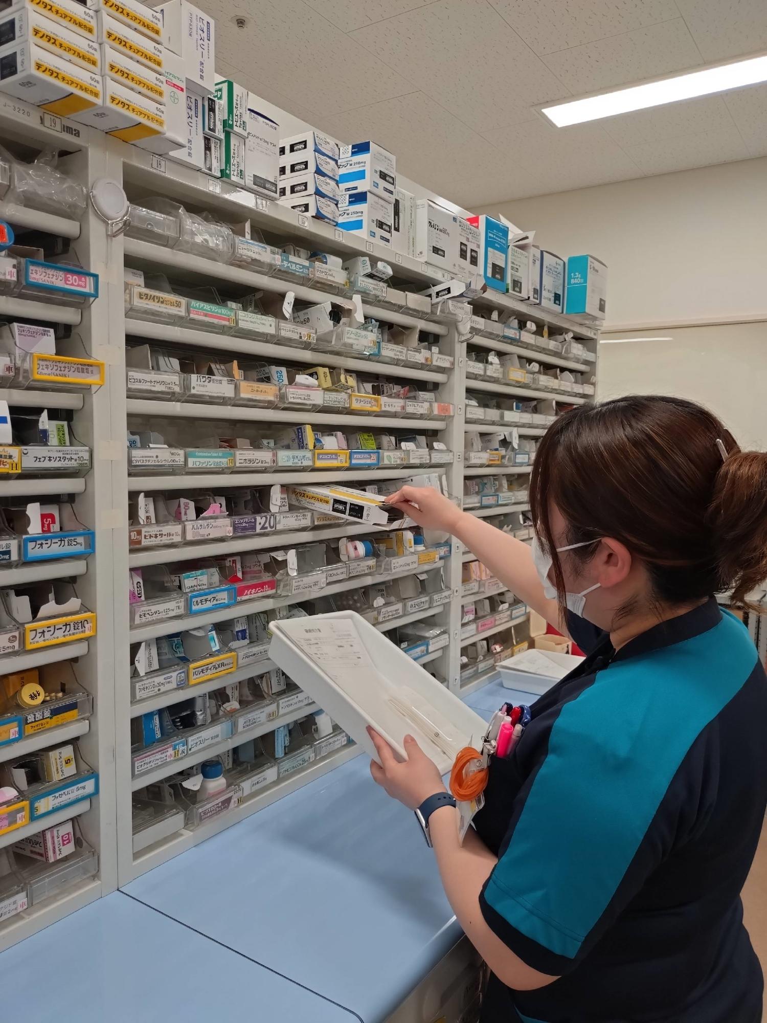 数多くの薬が入った棚から薬を取り出している女性の写真
