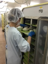 衛生キャップを付けた人が棚の中の料理を確認している写真