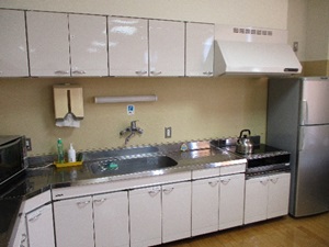 上部に棚がありコンロと流しの付いた白い台所の写真