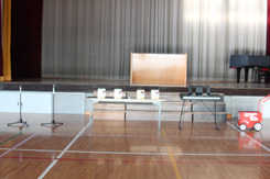 体育館内にテーブルや赤いラインカーなどの備品が並べられている写真