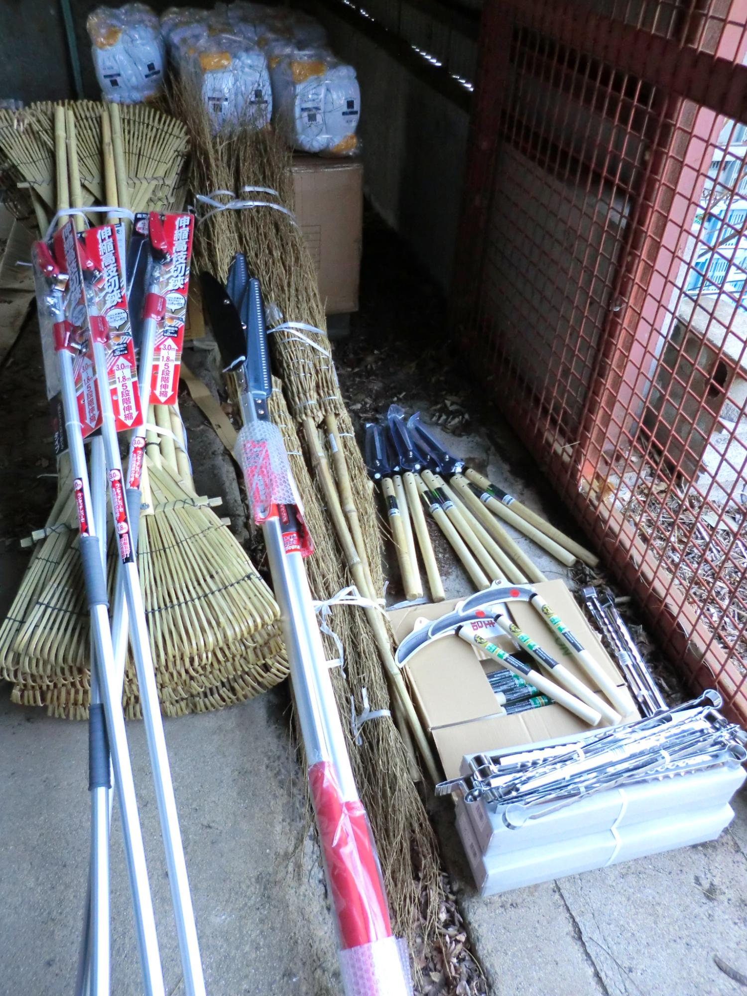 倉庫に清掃用の熊手や竹箒が並べられている写真