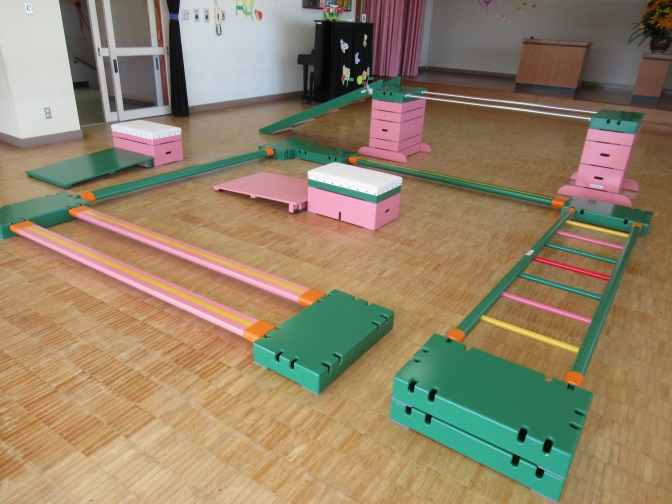 体育館のような場所に設置された平均台や跳び箱などの運動用具の写真