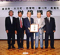 室内で「さぬき市」と書かれた額を男性たちが手で支えている様子の写真