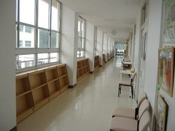 廊下の窓際に空の本棚が並んでいて反対側に読書用の椅子が置かれている写真