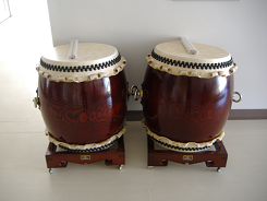 白い壁の角に二組の真新しい和太鼓の上にばちが置かれた写真
