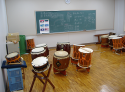 使い古された和太鼓とスタンドに置かれた締太鼓が多数置かれている部屋の写真