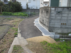 畑と家の間の道が舗装されている写真