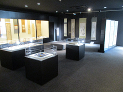 ガラスケースが並んだ黒い室内の展示室の写真