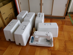 ケースに入ったミシンが床に並べられている写真