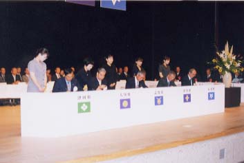 壇上にある白い布がかけられた机に座っている人たちの写真