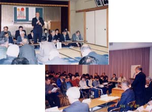 （上）和室のような部屋にスーツを着た人々が膝をついて座っている中で一人の男性が立っている写真（下）カーテンが閉められた室内にテーブルと椅子が置かれており人々が椅子に座っている写真