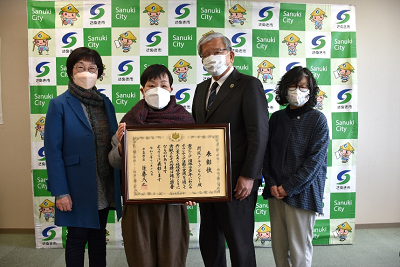 男女4人が並んで1人が表彰状を持っている記念写真