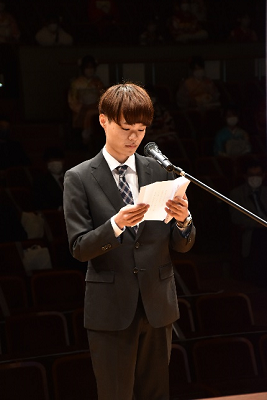 スーツを着用した男性が客席を背に話している写真