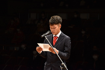 スーツを着用した男性が両手に持った紙を見ながら話している写真