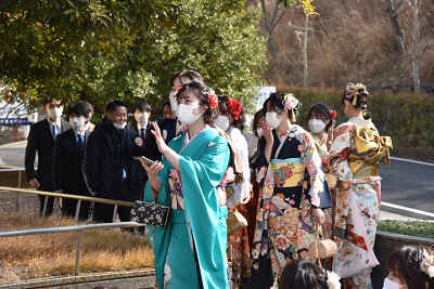 振り袖姿の女性やスーツ姿の男性が列になって歩いている写真