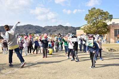 園児と向き合って、片腕を伸ばしたポーズをする女性の写真