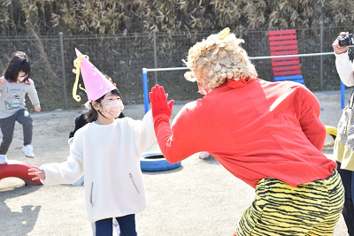 ピンク色の三角帽子を被った女子園児が赤い鬼の仮装をした人とハイタッチしている写真
