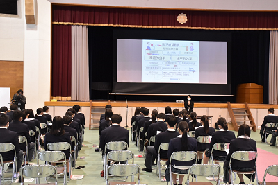 体育館で椅子に座ってスクリーンを見る生徒達