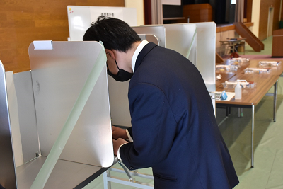 仕切りのついた記載台で投票用紙に書き込んでいる生徒の写真